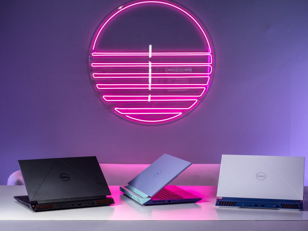 Three laptops on a table under a pink neon sign