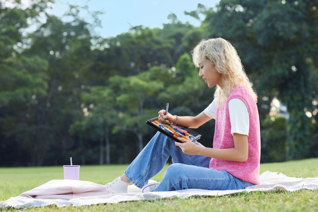 Woman sitting on a blanket on a lawn working on a 2-in-1