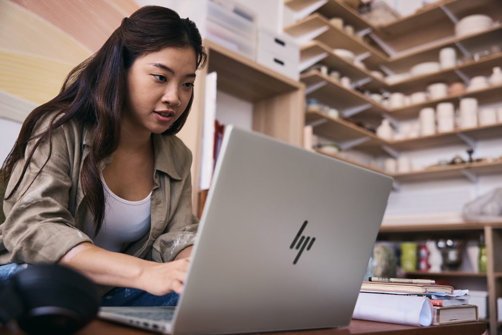 Woman working on an HP laptop in front of shelves of pottery